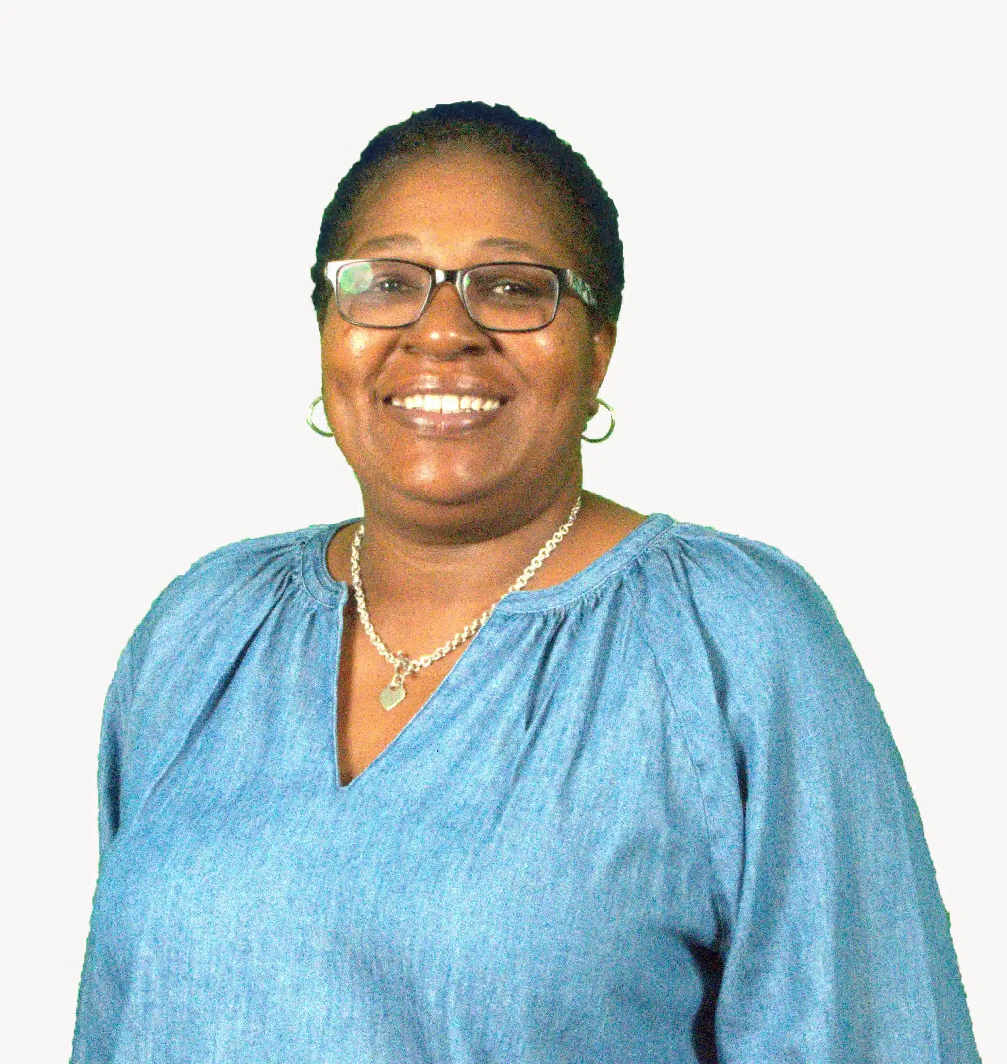 A person is smiling while wearing glasses, a silver necklace, and a light blue blouse, radiating a sense of calm reminiscent of the serenity found in pulmonary rehab. The background is plain white.