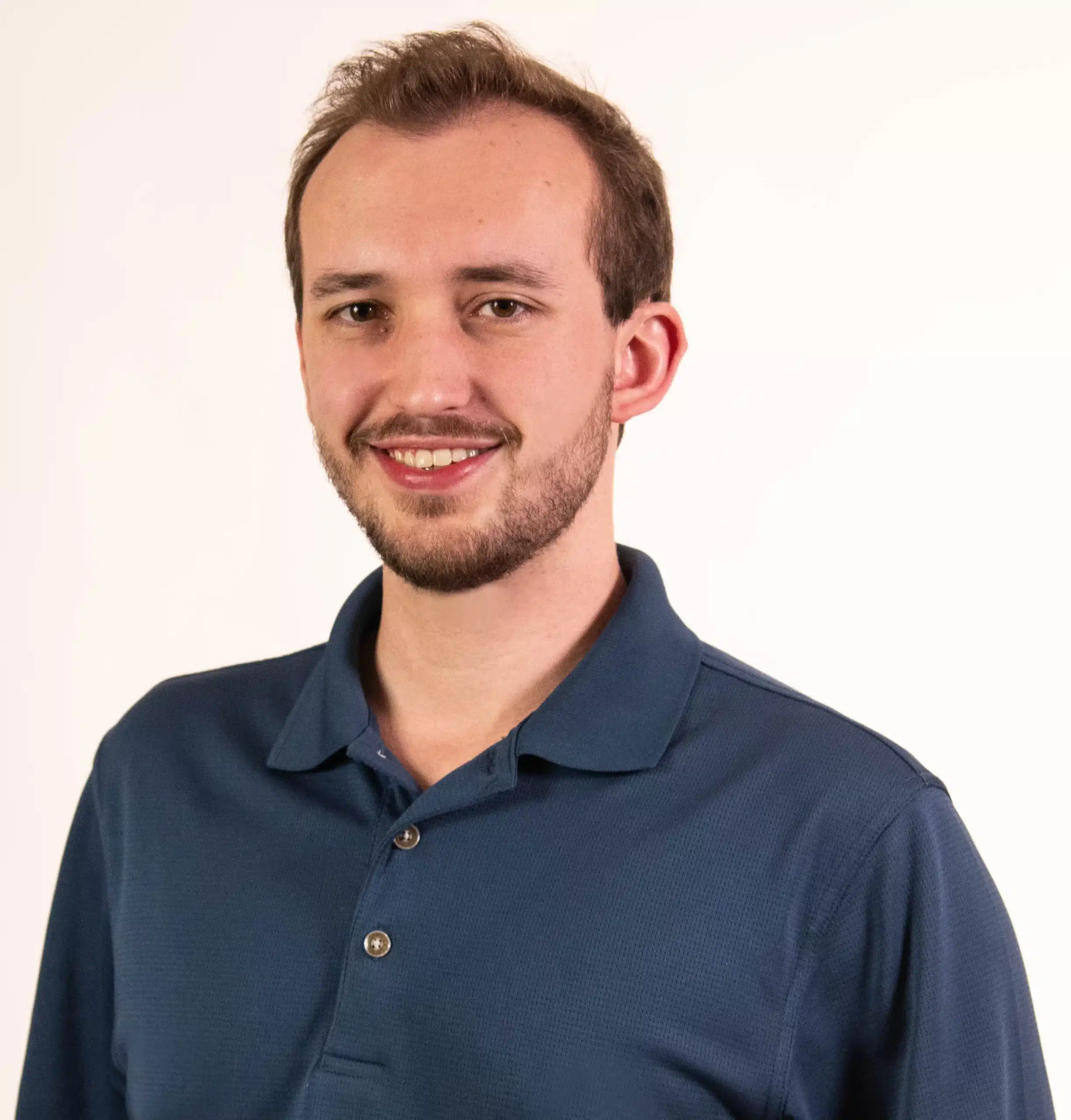 A person with short hair and a beard is smiling, exuding vitality in a blue polo shirt. They stand confidently against a plain white background, embodying the benefits of pulmonary rehab.