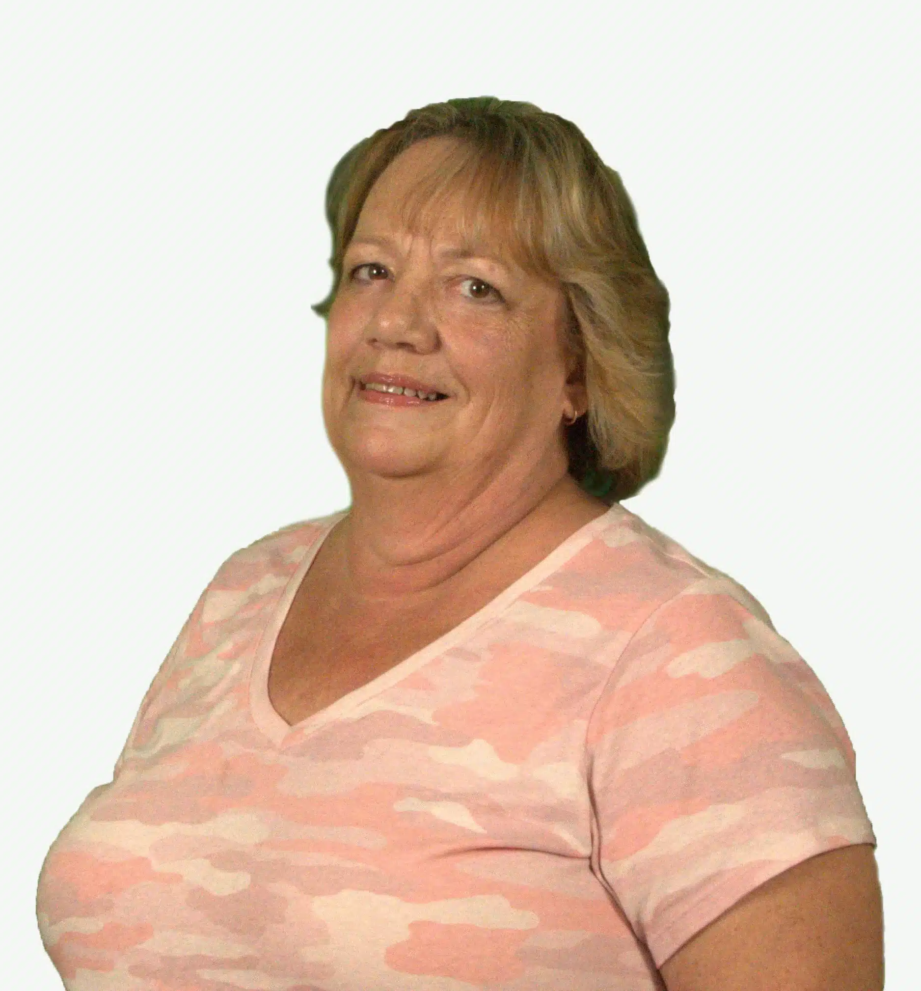 A woman with shoulder-length hair is smiling softly at the camera, her light pink and white camouflage-patterned T-shirt adding a touch of style. Against the solid light background, she exudes calm confidence, perhaps on her way to a pulmonary rehab session.