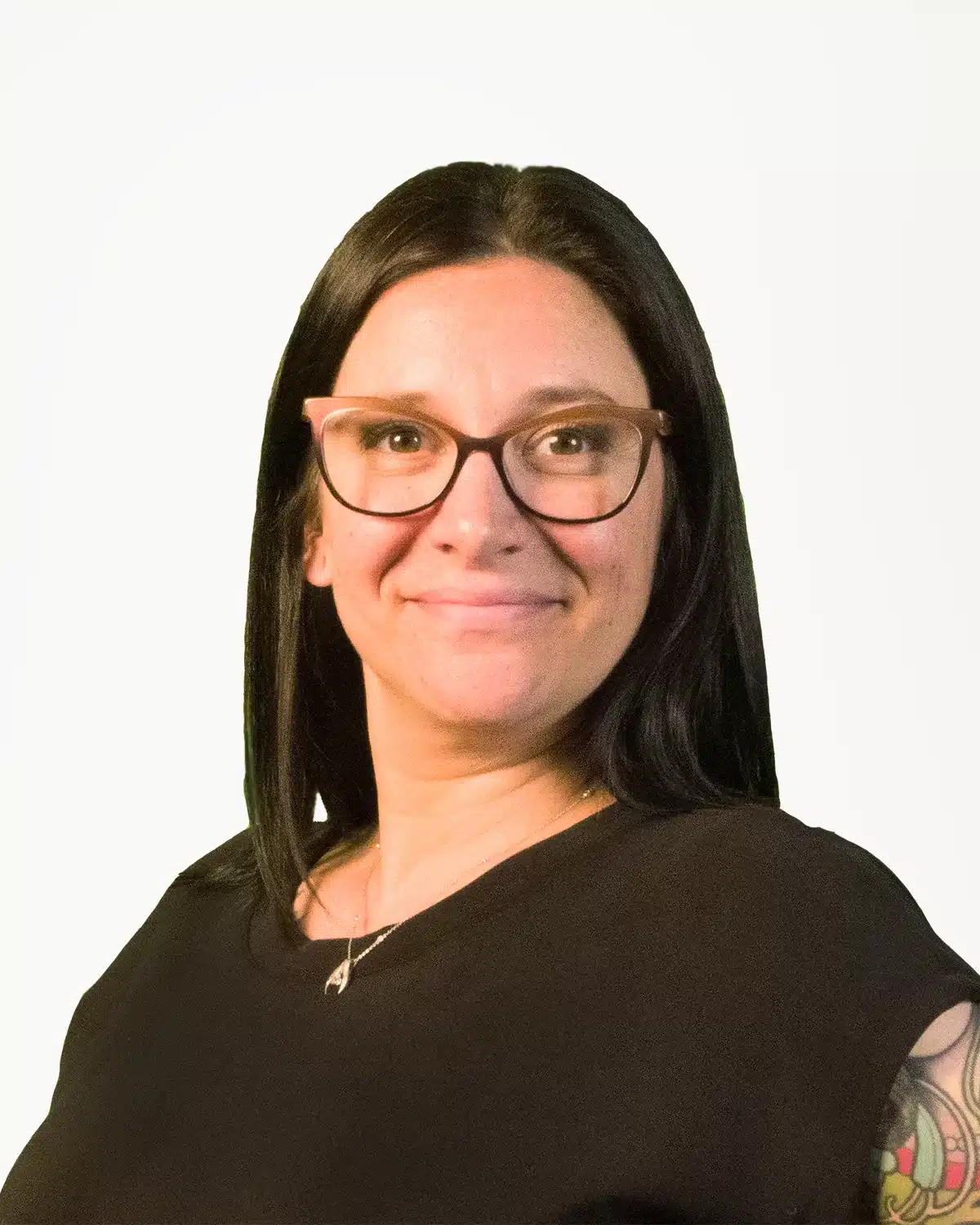 A woman with long black hair and glasses smiles at the camera, exuding warmth and confidence. She is wearing a black top, showcasing a tattoo on her right arm—a nod to her journey through pulmonary rehab. The background is plain and light-colored, highlighting her vibrant presence.