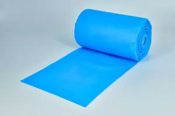 A roll of PT/OT Non-Latex Therapy Bands in bright blue is partially unrolled on a plain white surface, appearing smooth and reflective, with the roll standing upright on one end.