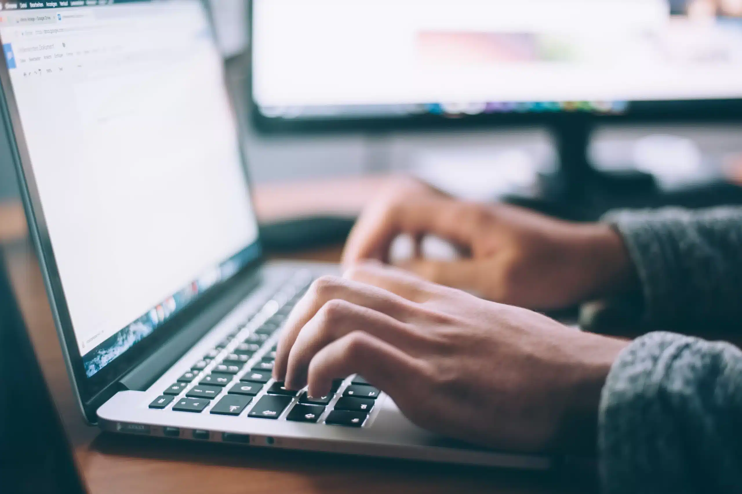 Hands typing on a laptop keyboard, with a blurred computer screen in the background, suggesting focused work or study on pulmonary rehab in a quiet indoor setting.