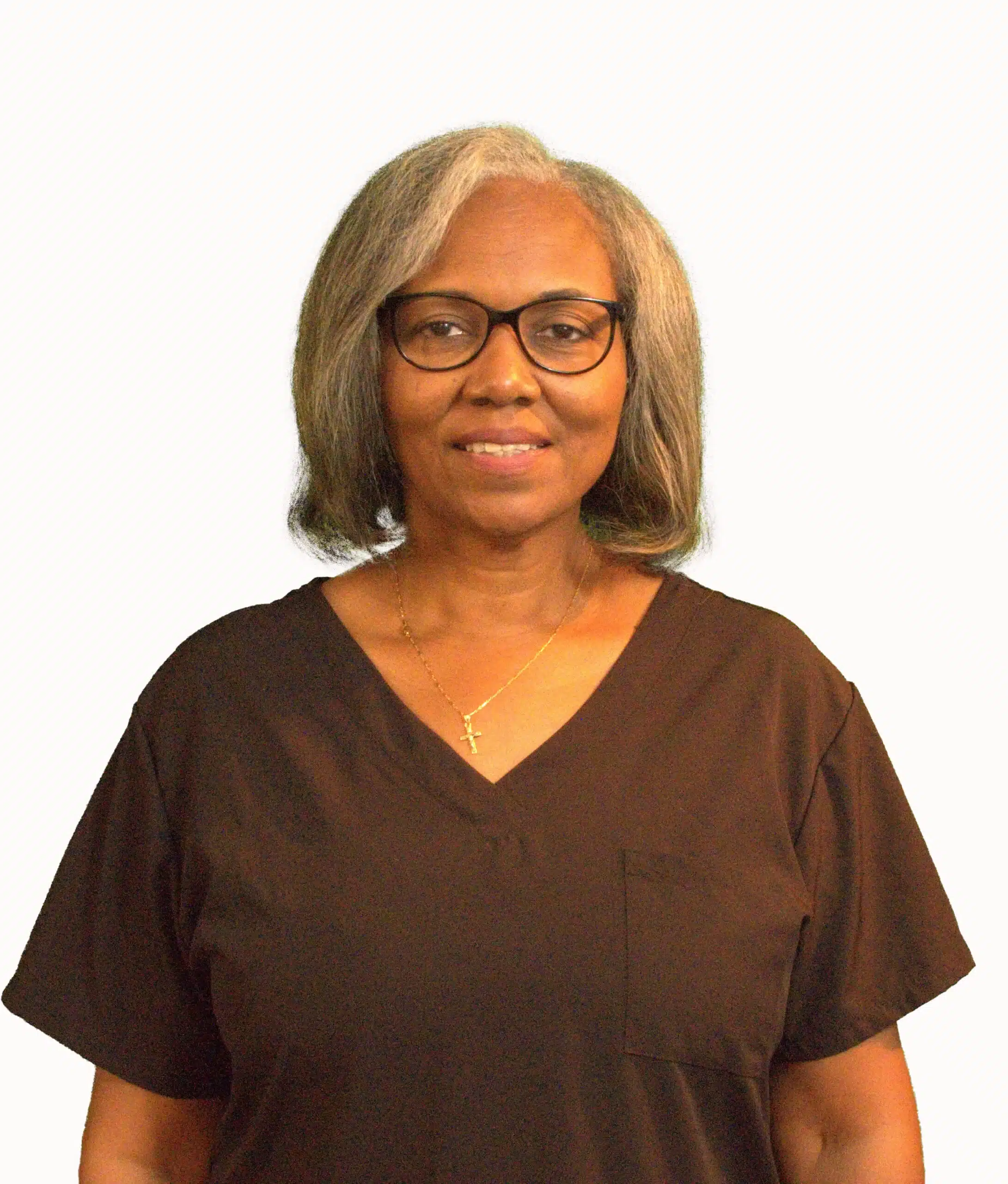 A smiling woman with glasses, shoulder-length gray hair, and a gold necklace with a cross pendant stands confidently. Clad in black scrubs, she embodies the dedication of those in pulmonary rehab against a plain white background.